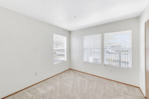 Interior Unit Bedroom, neutral toned carpeting, white walls, three windows.