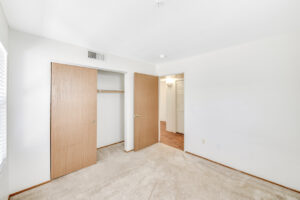 Interior Unit Bedroom, Neutral toned Carpeting, sliding closet door, wood floors in hallway, white walls.